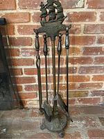 Full view of the vintage brass fireplace tool set standing on a brick hearth. Includes poker, brush, shovel, tongs on stand with ship topper.