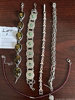 Photo showing five distinct bracelets laid out on dark wood surface for scale and detail.