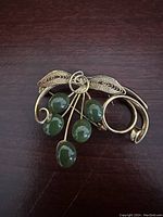 Vintage gold-tone filigree pin with five green cabochon stones on dark wood background.