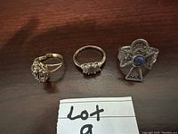 Top view of three silver ladies' rings on dark wood surface: one with a large silver filigree Ankh and lapis stone, one with amethyst cluster, and a three stone clear gemstone ring.
