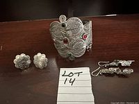 Photo showing silver filigree bracelet with colored stones along with two pairs of silver earrings: a pair of clip-ons and a pair of drop earrings.