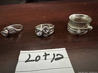 Three silver ladies rings laid out with a handwritten 'Lot 12' note, showing the different styles and gemstone settings.