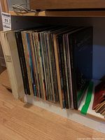 Photo of multiple vinyl record albums stacked vertically on a shelf, showing spines and partially visible covers.