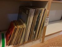 Multiple vinyl LP albums stored upright on a wooden shelf, showing a collection of various artists' records.