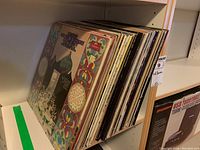 Side view of a shelf with a vertical stack of vinyl record albums with colorful covers including Fleetwood Mac and others.
