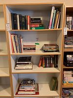 Four shelves of books, mix of paperbacks and hardcovers, showing a variety of titles and genres including history and quilting books.