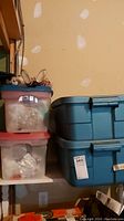 Plastic storage bins with Christmas ornaments wrapped inside, stacked on shelf