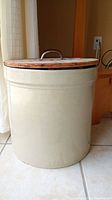 Full view of beige ceramic crock with wooden lid and metal handle, showing size and overall condition.