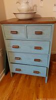 Front view of the wood dresser showing the five drawers with wooden handles, blue painted body, and natural wood top.