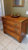 Oak dresser with three drawers seen from an angle, showing brass handles and wood grain.