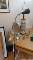 Full view of the three items on a wooden table: make-up mirror, gooseneck floor lamp, and artisan table lamp