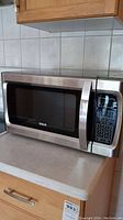 RCA stainless steel microwave oven on kitchen countertop showing door and control panel.