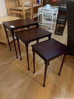 Three dark wood wooden nesting tables shown from side angle displaying their sizes and design with rounded feet finishing the legs