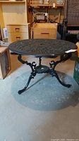 Front angle of the round metal patio table showing legs and tabletop detail.