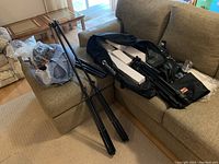 Black equipment bag containing light stands and white bulb boxes on couch