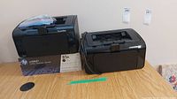 Two HP LaserJet P1102w printers side-by-side with one sealed HP 85A toner cartridge pack beside them, showing general lot contents.
