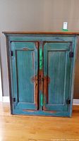 Front view of the rustic wooden cabinet showing two paneled doors with distressed turquoise paint and a wooden top.