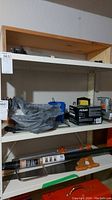 Shelf with items including a Black and Decker sander box, plastic containers, and assorted tools in basement setting.