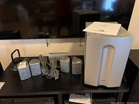 Overall setup showing two satellite speakers, center speaker, subwoofer, and wiring on a table.