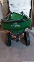 Front view of Scotts Turf Builder EdgeGuard Mini walk-behind spreader showing green hopper and wheels.