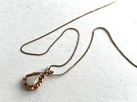 Full view of 14K gold chain with textured gold opal pendant in pear shape on white background.
