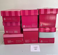 Stack of seven pink-striped Marie Osmond doll boxes showing Fire Collection branding and product details on sides.