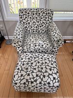Front view of the floral patterned armchair with matching ottoman in front of it on hardwood floor near a window.