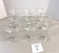 Group of nine clear crystal champagne coupe glasses arranged in three rows.