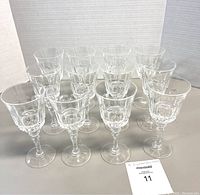 Eleven clear crystal wine glasses displayed in rows, showing detailed cut design and shape.