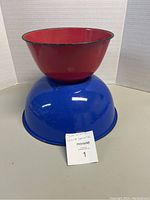 Photo showing stacked red and blue vintage enamel mixing bowls on a white surface with white backdrop.