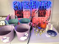 Wide shot of lot contents showing neon Halloween signs, pastel Easter baskets with bunny appliques, Dresden angels, pumpkin candle, and small decor items on a table.