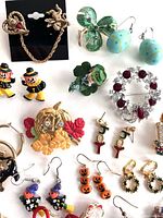 Close-up photo highlighting individual pieces such as pumpkin earrings, Santa earrings, Christmas candy cane earrings, and other holiday brooches.