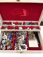 Open jewelry box showing red velvet lining with many costume jewelry pieces inside separated by compartments
