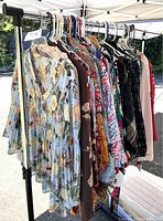 Photo showing multiple ladies tops hanging on a rack, including floral and solid color tops in various colors such as blue, brown, black, and pink.