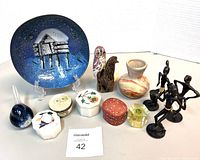 Photo shows the entire lot including a large decorative blue plate with a hut design, carved wooden owl figurines, various trinket boxes, a small marbled vase, small glass objects, and several dark figurines.