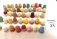 Photo of multiple vintage plastic advertising thimbles in various colors with printed promotional text, arranged in rows.