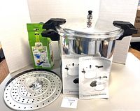 Mirro pressure cooker/canner with two perforated inserts, green boxed accessory item, instruction manual, and recipe booklet displayed together