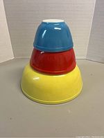 Stacked view of three Pyrex mixing bowls in blue, red, and yellow showing overall shape and colors.