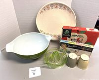 Photo shows all items together: green and white Pyrex bowl, glass reamer, two shakers, boxed thermometer set, boxed apple parer corer, and beige Franciscan platter with fruit pattern near edge.