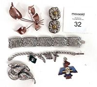 Full view of the jewelry lot arranged with flower brooch, cat brooch, wide detailed silver bracelet, charm bracelet with several charms, and rectangular flower earrings.