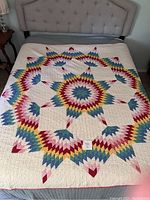 Full view of the vintage Broken Star quilt laid out on a bed showing vibrant multicolor star pattern on a cream background.