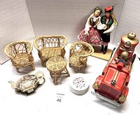 Overview of vintage toys including red fire truck, wicker miniature furniture, dolls, pin container, and a small figurine tray.