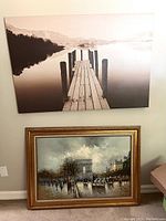 Photo showing the two wall art pieces hung side by side on a wall: the canvas print with wooden dock above and the framed oil painting below.