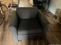 Two views of one of the dark patterned fabric upholstered armchairs showing rounded arms and cushioned seat and back.