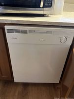 Closed front view of Frigidaire dishwasher installed under countertop, showing clean white exterior with control knob and button.
