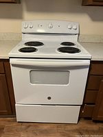 Front view of the white GE electric stove showing four coil burners, oven door with window, and control knobs.