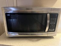 Front view of a Magic Chef stainless steel microwave showing the door and digital keypad on the right.