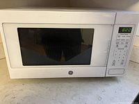 Closed view of GE white microwave oven showing keypad and digital clock at 8:20.
