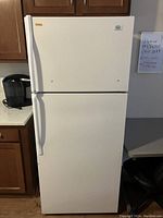 Full view of the white Roper by Whirlpool refrigerator with top freezer, placed between kitchen cabinets.