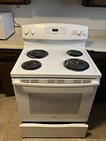 Photo of white GE electric stove with coil burners on stovetop and oven door with glass window, showing control knobs and digital display panel.